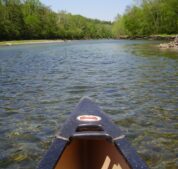 The tip of a canoe overlooks the White River with crystal clear waters and lush green foliage.