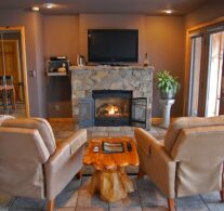A warm fire in the native stone fireplace with the 4K TV above and two comfortable recliners in the foreground. The lake view is just to the right and can be seen anytime.