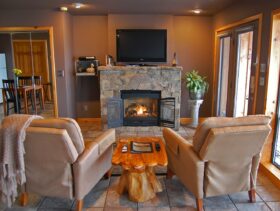 A warm fire in the native stone fireplace with the 4K TV above and two comfortable recliners in the foreground. The lake view is just to the right and can be seen anytime.
