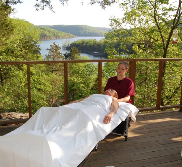 One of our professional masseuses gives a relaxing massage on the outside deck of a cabin with the peaceful scene of the lake and forest as the backdrop.
