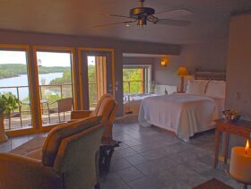 Recliners and a romantic candle in for ground with the queen-sized bed, Jacuzzi, and wall of windows overlooking Beaver Lake making up the background.