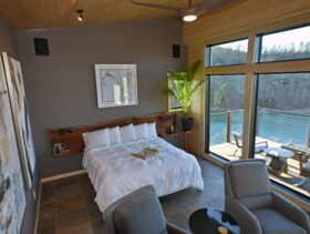 An interior view looking down on the 'art wall' on the left, king-size bed in the middle, and ten and a half foot high windows overlooking Beaver Lake and the suspended balcony.