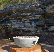 The bluff cabins's round, stone-facade, fire table on it's octagonal base with the 14' natural bluff in the background.