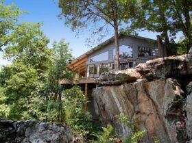 The front, glass wall and surrounding trees and bluffs of one of our Beaver Lake Cabins as seen from the exterior.