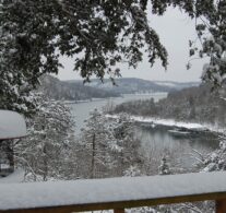 A snow-covered railing in the foreground underscores a winter wonderland with Beaver Lake in the distance.