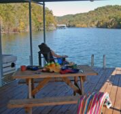 A women looks out at the rippled lake in an adorondack chair on the edge of the dock. A table under the covered area of the dock is set up for a nice picnic.