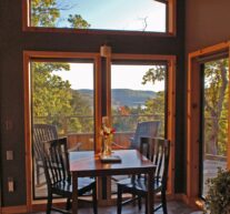Late-afternoon light illuminates the cabin's dining table and its' forest-bounded view of Beaver Lake through the large, front wall windows.