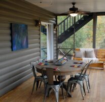 A large screened in porch where an outdoor dining table and rocking bench adorned with pillows and blankets are awaiting you along ceiling fans that provide a steady breeze.