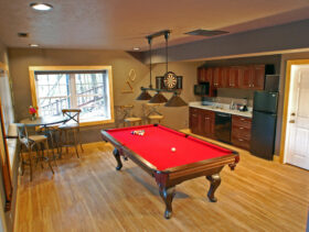 Looking into the lake house's downstairs game room equipped with red felt slate pool table and boars hair dartboard for hours of fun. A large kitchenette with full-sized fridge, microwave, dishwasher, and blender with bar tools all there for ease of enjoyment.