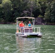 A happy couple enjoying a leisurely boat ride on our rentable mini electric pontoon featuring a shade canopy for relief on a hot sunny day.