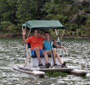 Two guests smiling and waving as they pedal along on Beaver Lake in our complimentary pedal boat.